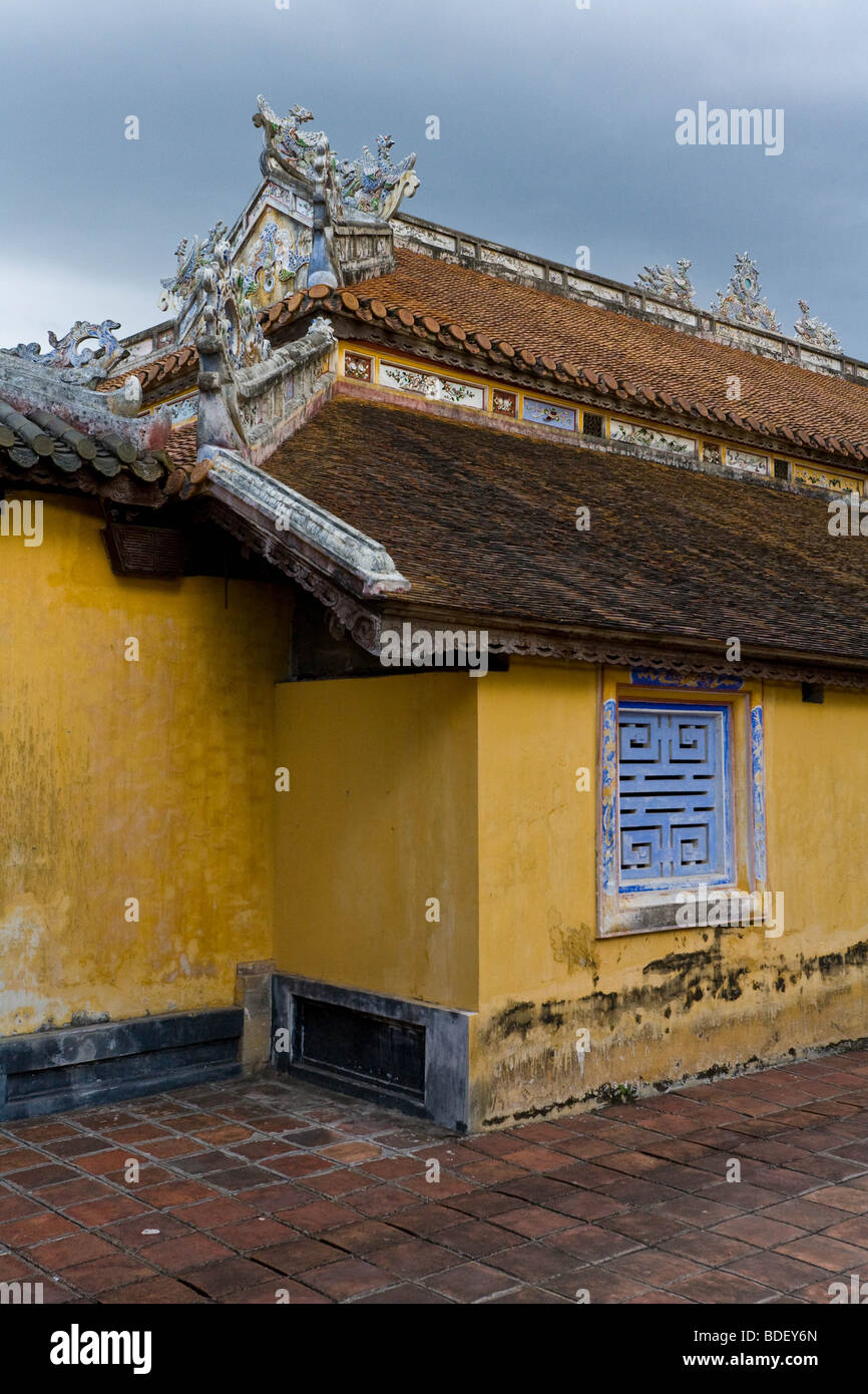 A yellow building of the palace at Hue, Vietnam, with intricately carved edges to the brown tile roof Stock Photo