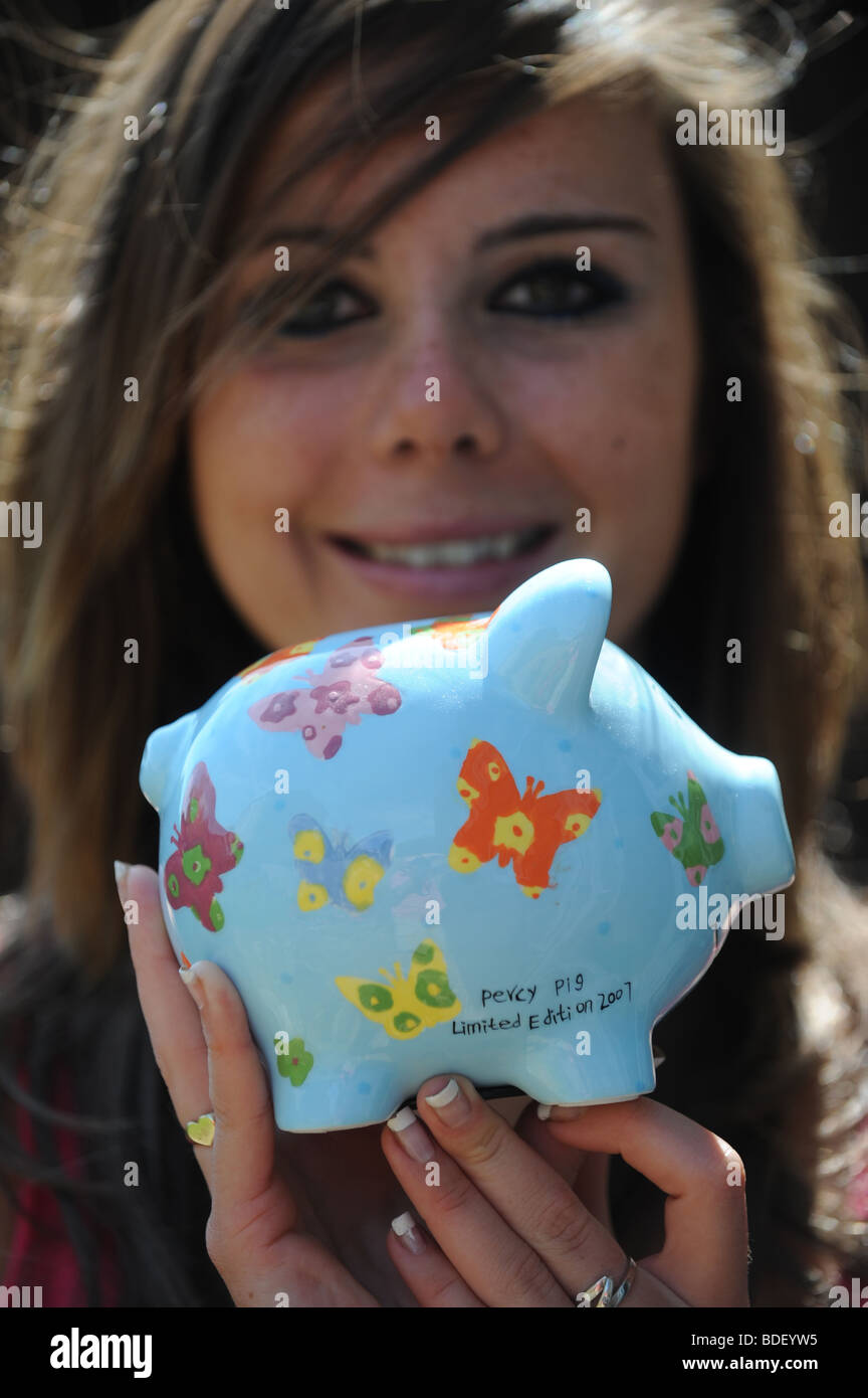 Pretty girl young woman holding Percy Pig blue piggy bank with painted butterflies on Stock Photo