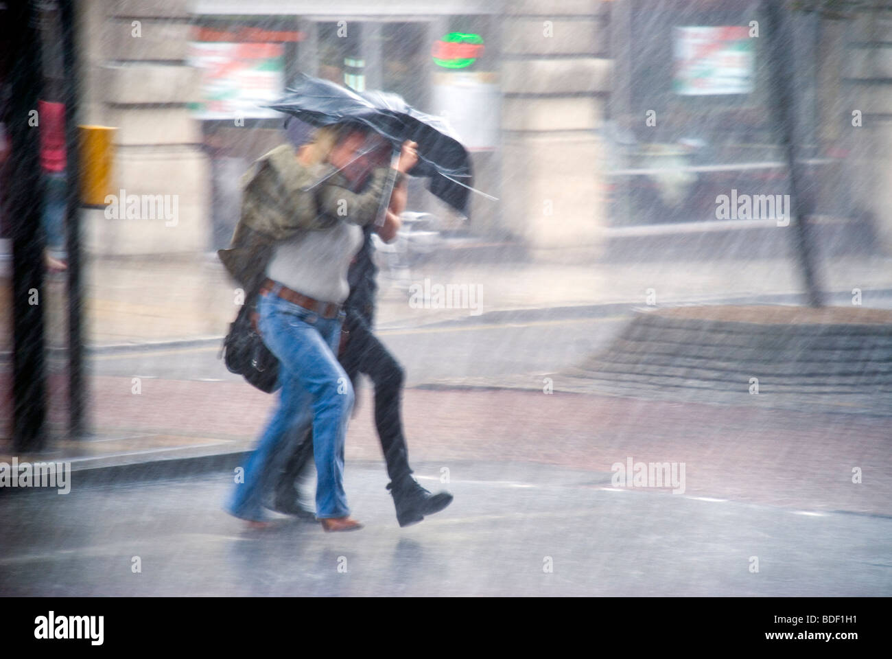 Two women share broken umbrella in a flash storm in the city Stock Photo