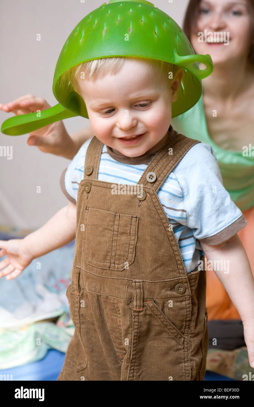 mother put colander on head of her little smiling baby one years old ...