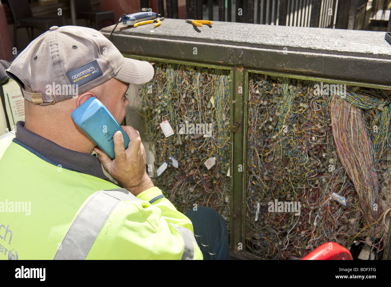 Looking over the shoulder of BT telecommunications engineer on phone infront of open wiring junction box on street Stock Photo