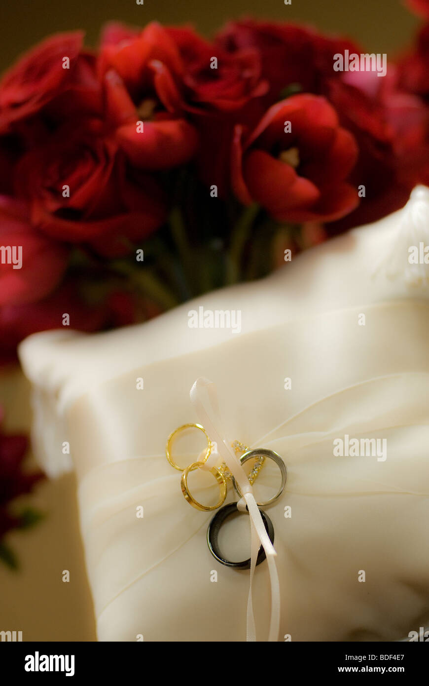 Wedding rings on a wedding ring cushion with a bouquet of red roses in the background. Stock Photo