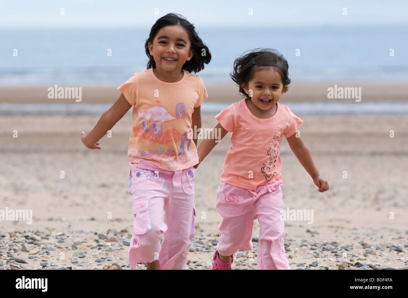 Two girls running in the beach holding hands Stock Photo - Alamy