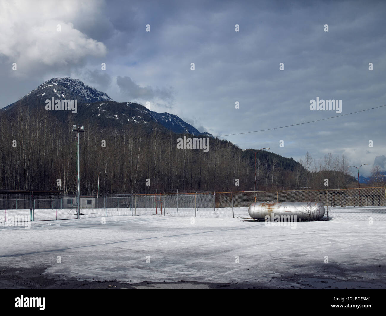 Vacant snow covered industrial lot with propane tank, chainlink fence