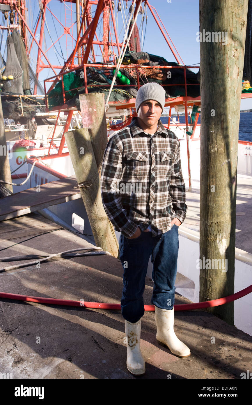 Young fisherman in hat standing in front of fishing boat Stock Photo