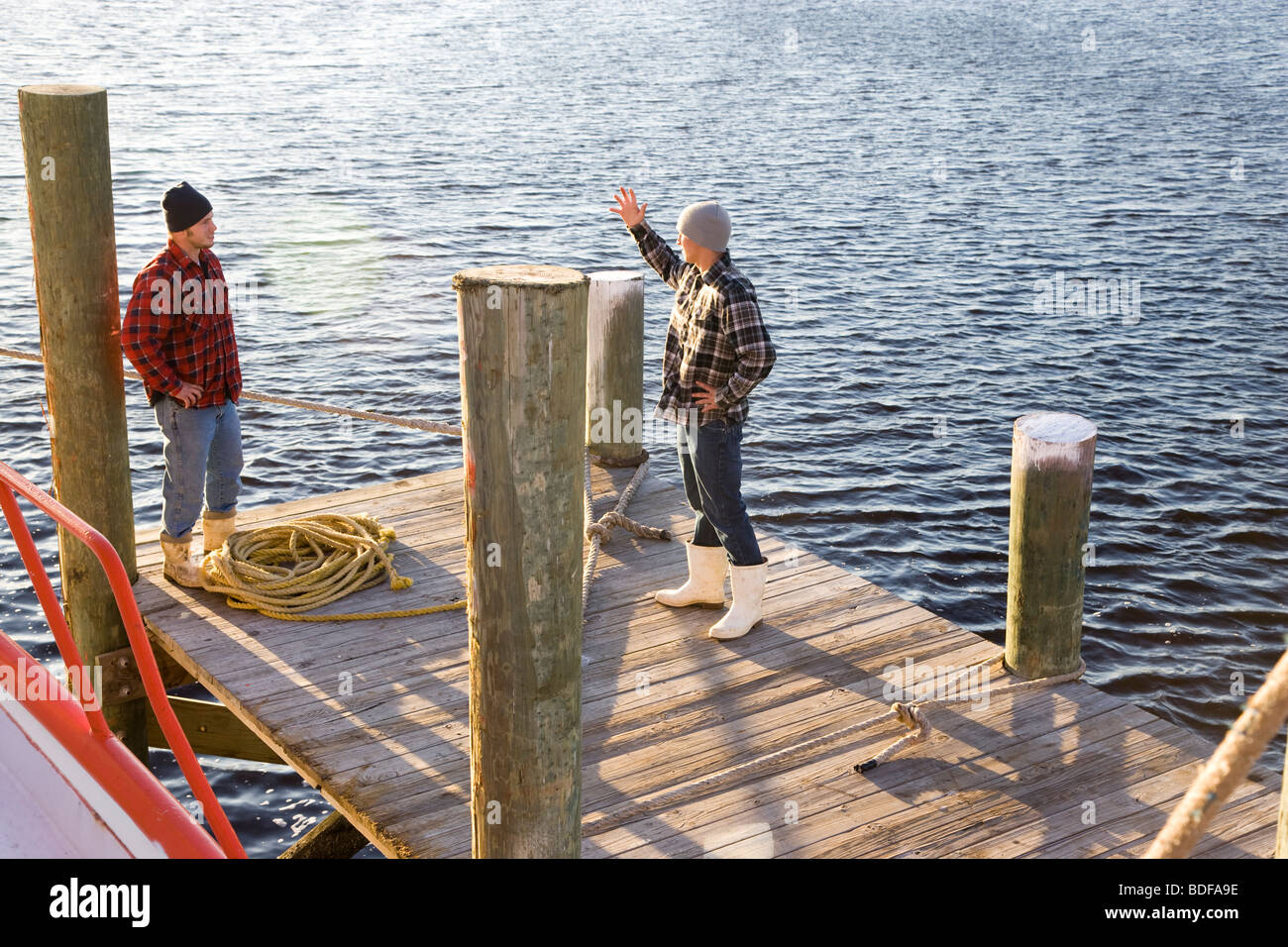Young fishermen in plaid shirts standing on pier with rope near fishing boat Stock Photo
