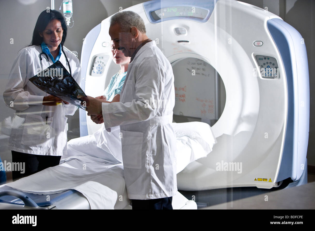 Radiologists looking at test results with patient near CT scanner Stock Photo