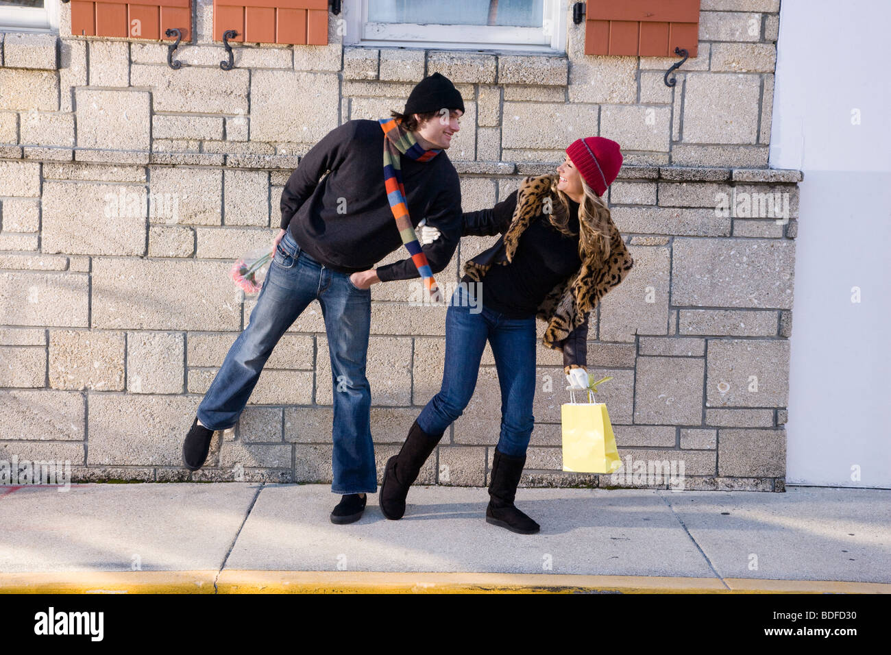 Young woman in warm clothes pulling boyfriend along sidewalk Stock Photo