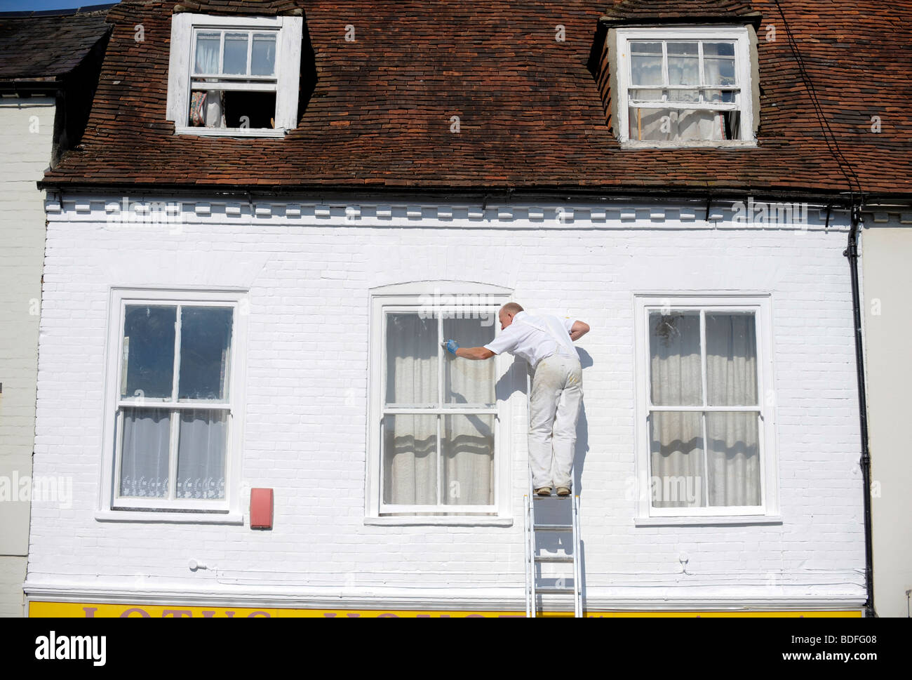 A man high up a ladder painting a window in Chichester, West Sussex, UK. Picture by Jim Holden. Stock Photo