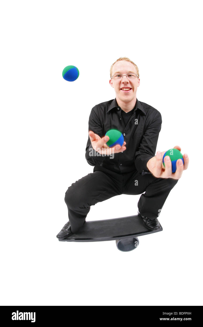 young man juggling with balls and balancing on a rola bola balance