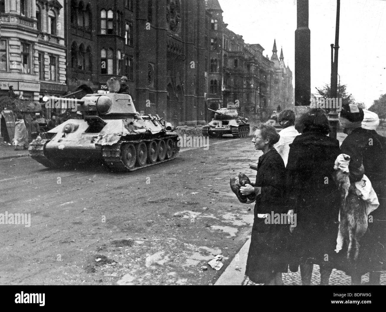 RUSSIAN TANKS enter a ruined Berlin in 1945 watched by an apprehensive group of women Stock Photo