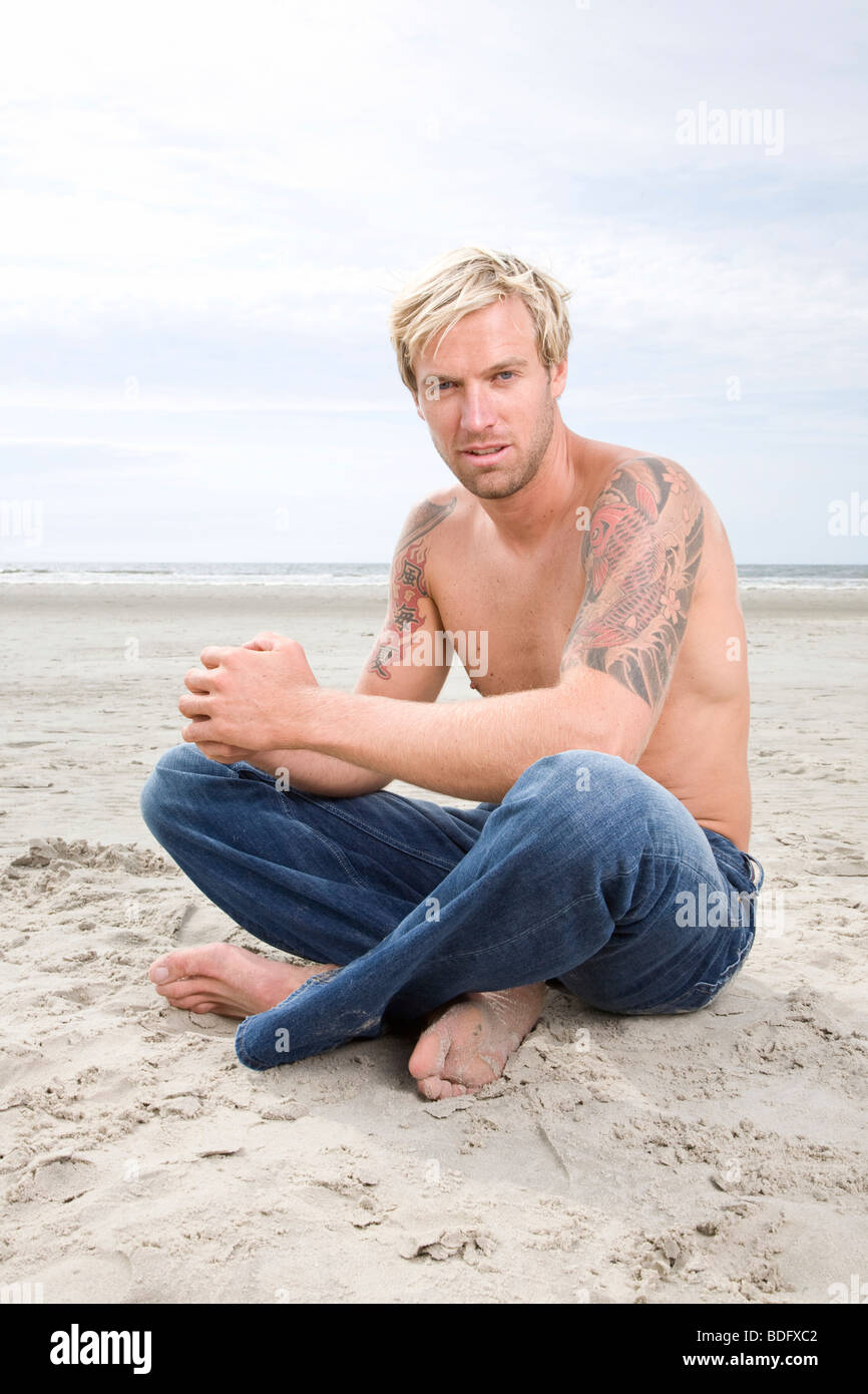 Young man sitting on the beach with open chest Stock Photo