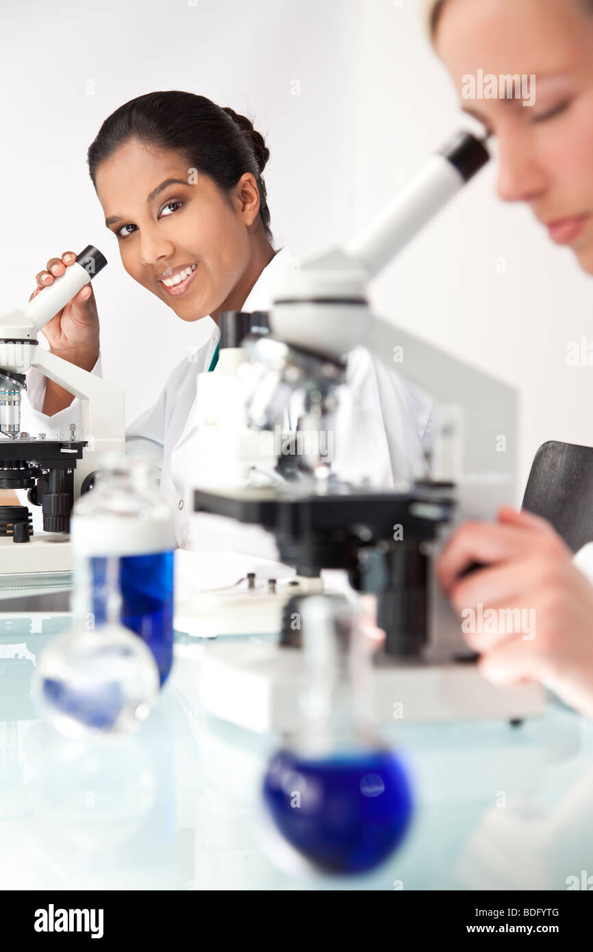An Asian female medical scientific researcher or doctor using her microscope in a laboratory with her colleague Stock Photo