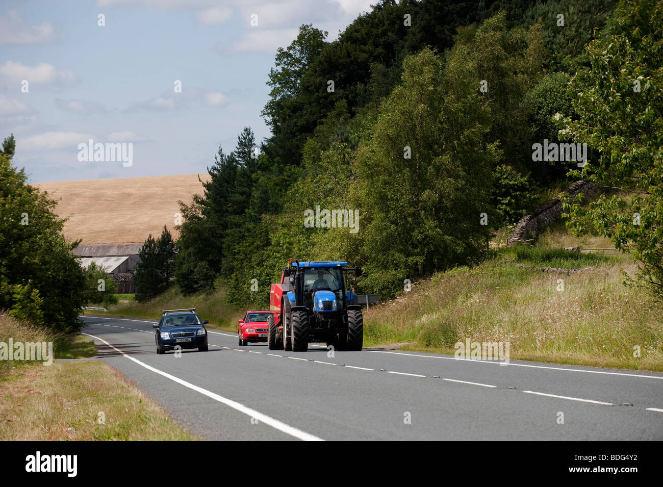 New Holland tractor being overtaken on rural road. Cumbria. Stock Photo