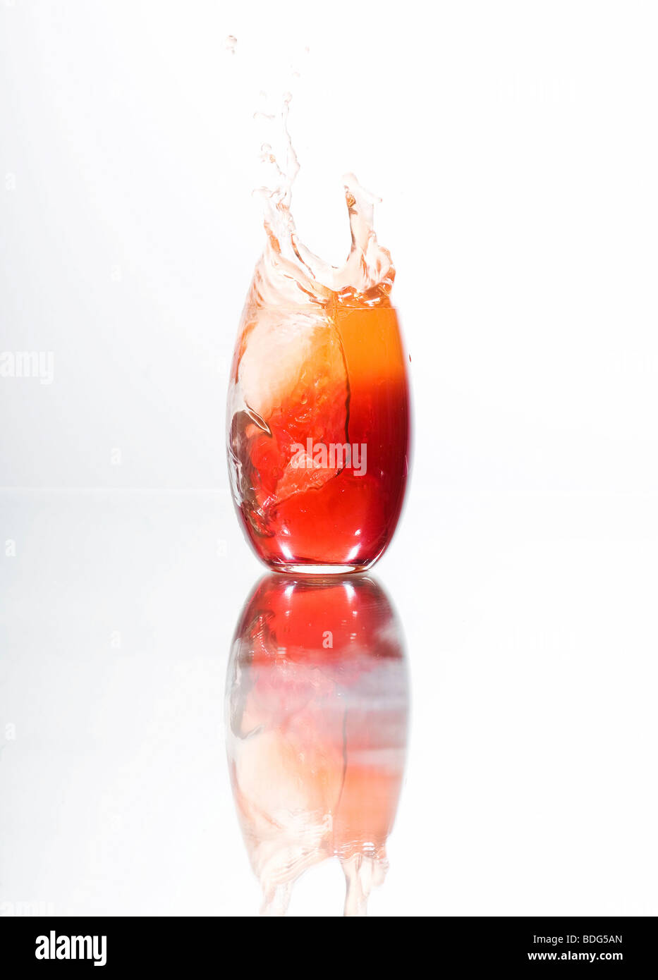 Ice cubes falling into a glass filled with red liquid Stock Photo