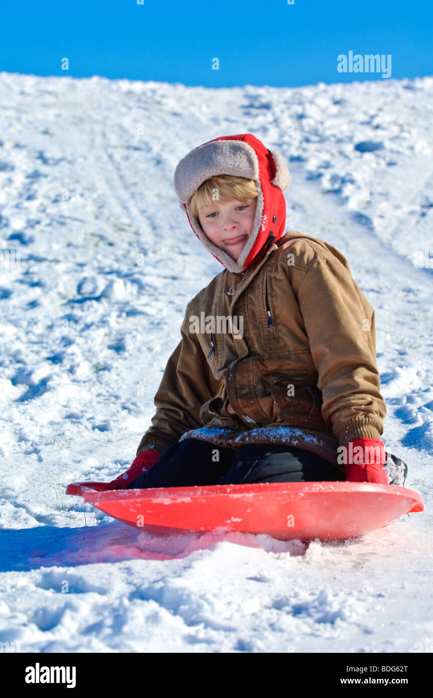 A boy sleds down a snowy hillside under a clear blue Wisconsin winter sky. Stock Photo