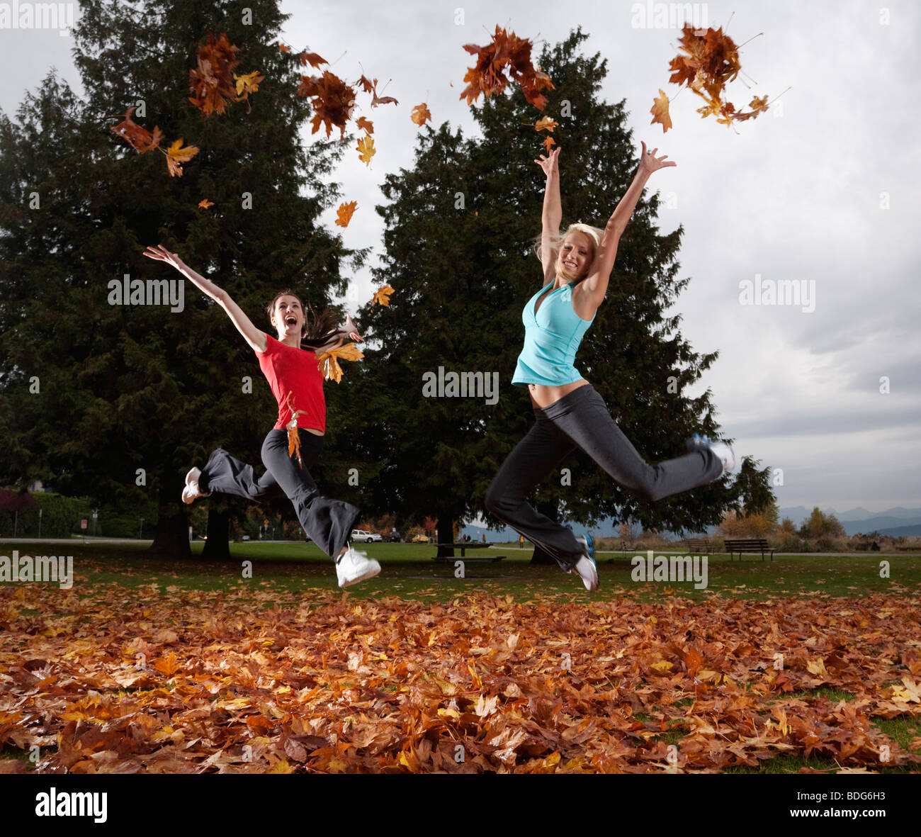 Two young cheerleaders do cheers with handfuls of autumn leaves