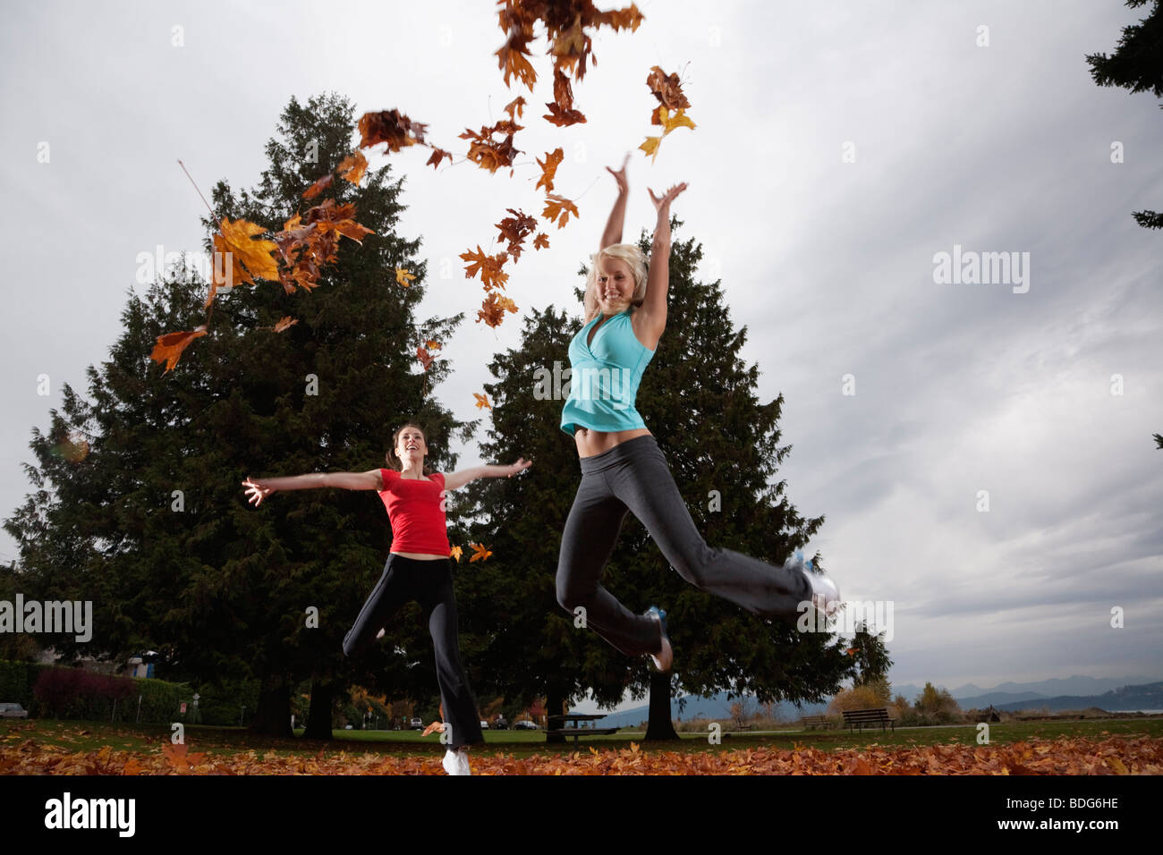 Two young cheerleaders do cheers with handfuls of autumn leaves