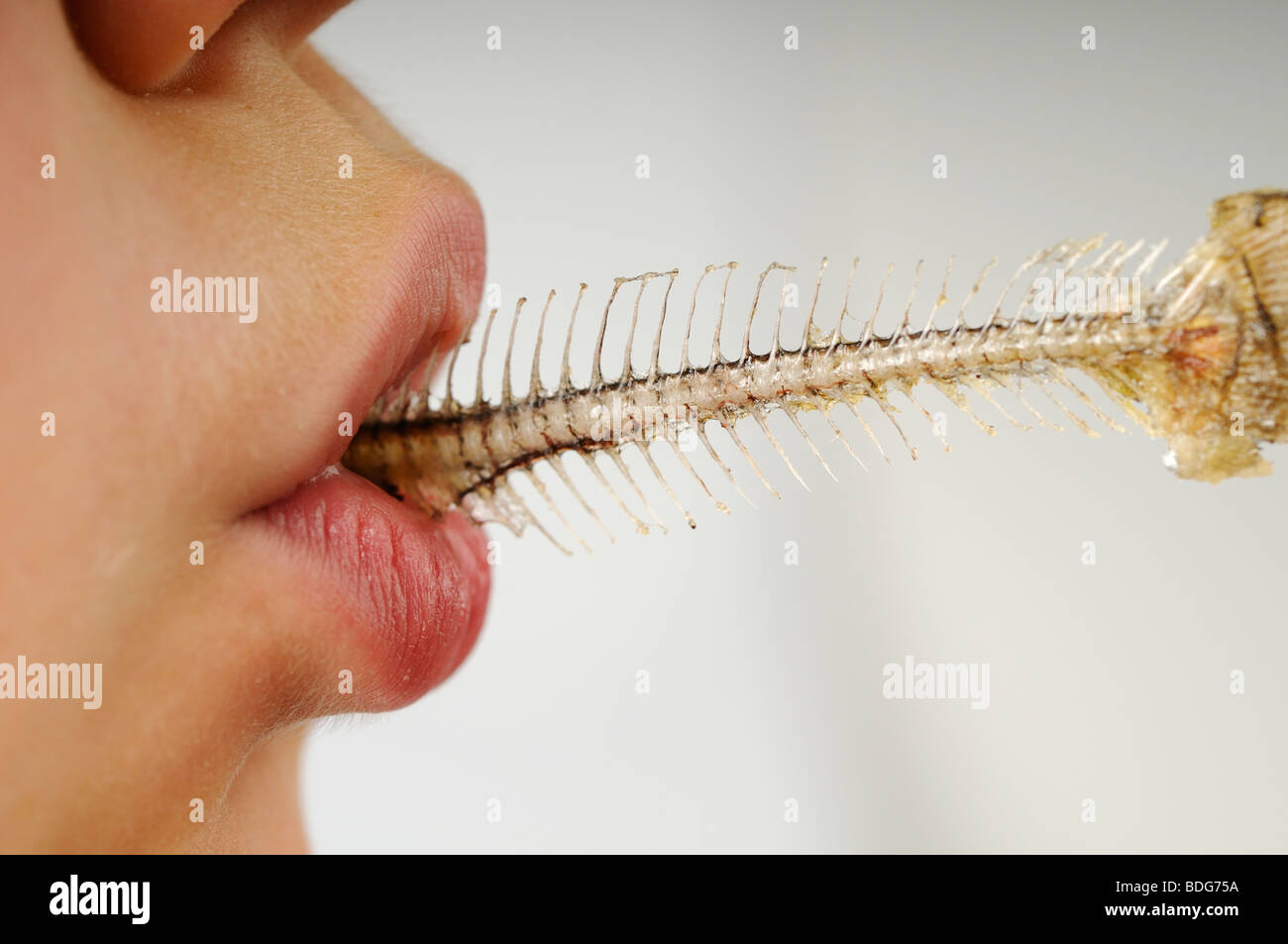 Stock photo of a young boy sucking clean the last pieces of meat from a fish skeleton. Stock Photo