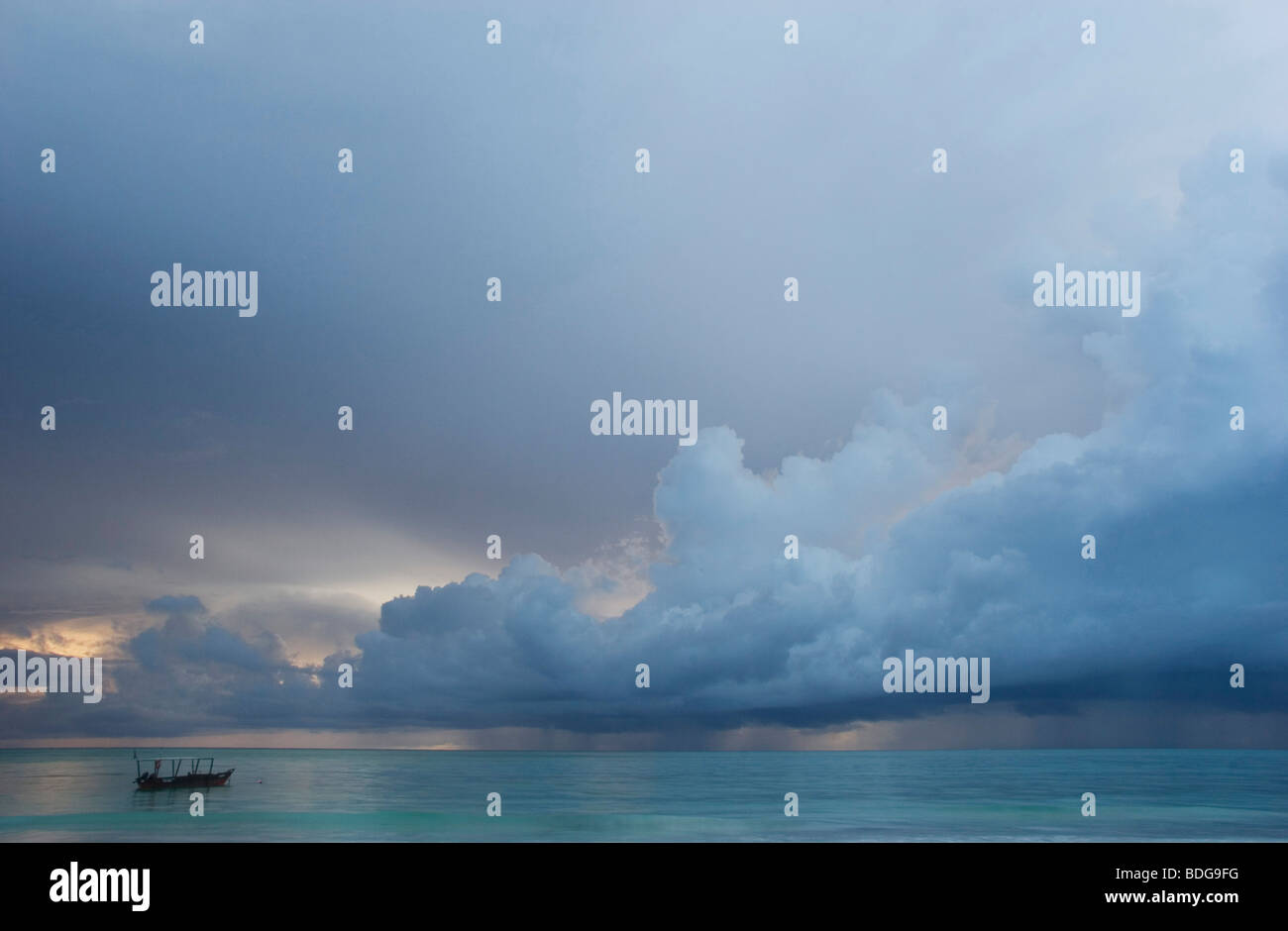 Diving boat floats in the ocean, just off the coast at Paje  Beach. At sunrise with billowing clouds tinged with blue. Stock Photo