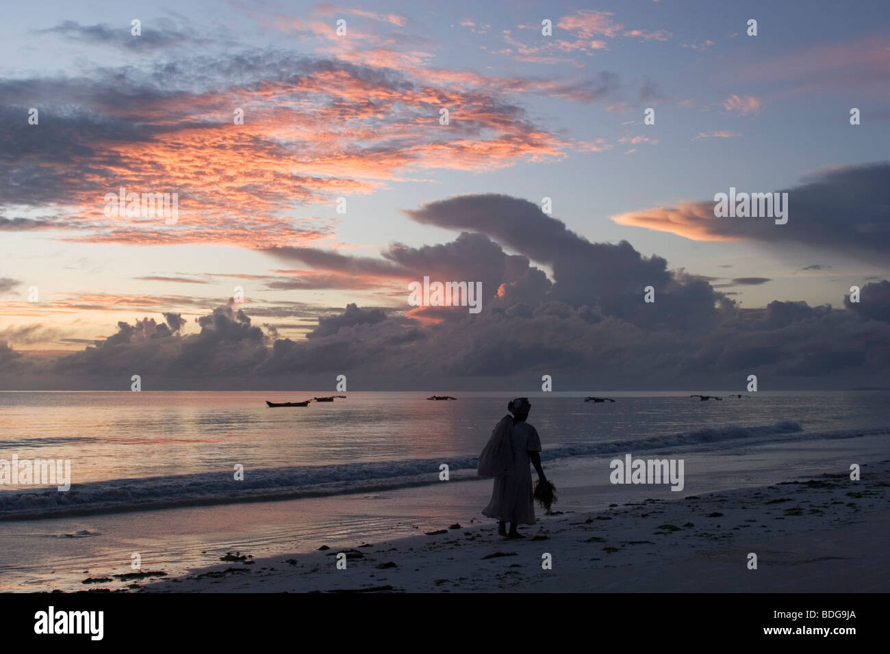 The lone figure of a woman at dawn. Sunrise over the ocean, on the coast at Paje beach, Zanzibar. Stock Photo