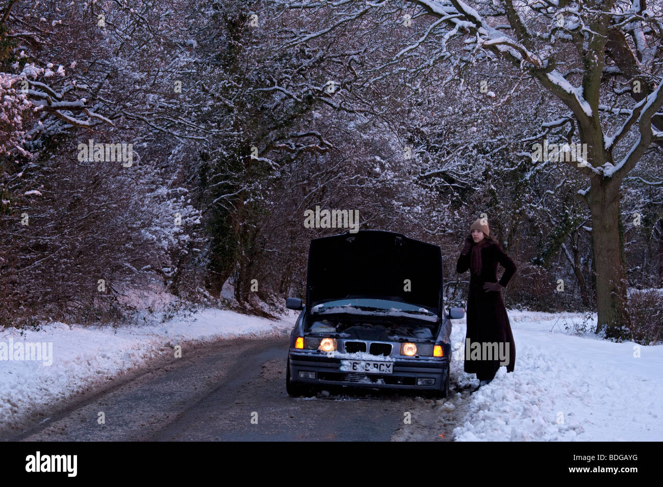 Women on her own with broken down car in the snow,stranded trying to get it fixed. Stock Photo