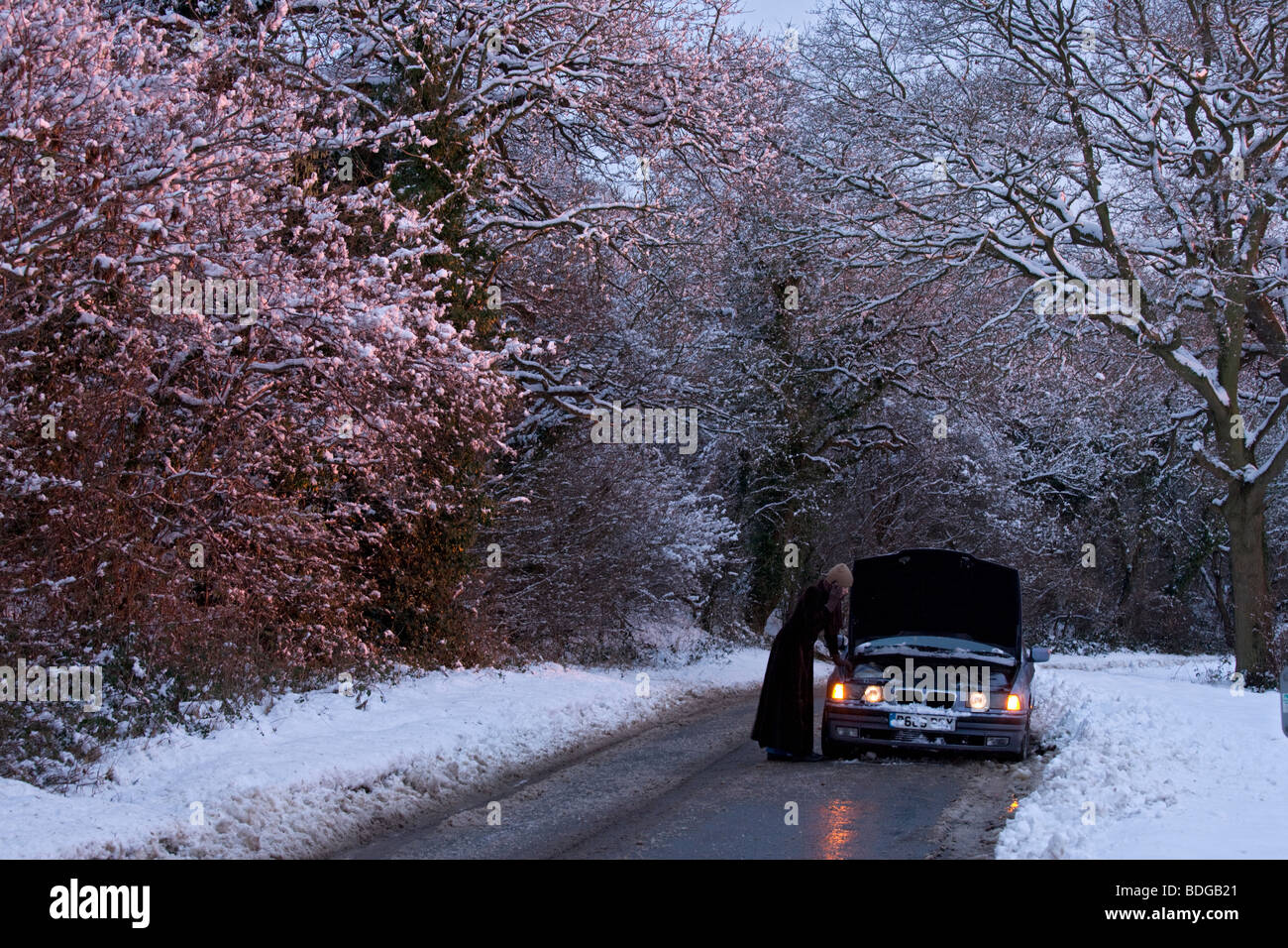 Women on her own with broken down car on country road in the snow, stranded trying to get it fixed. Stock Photo