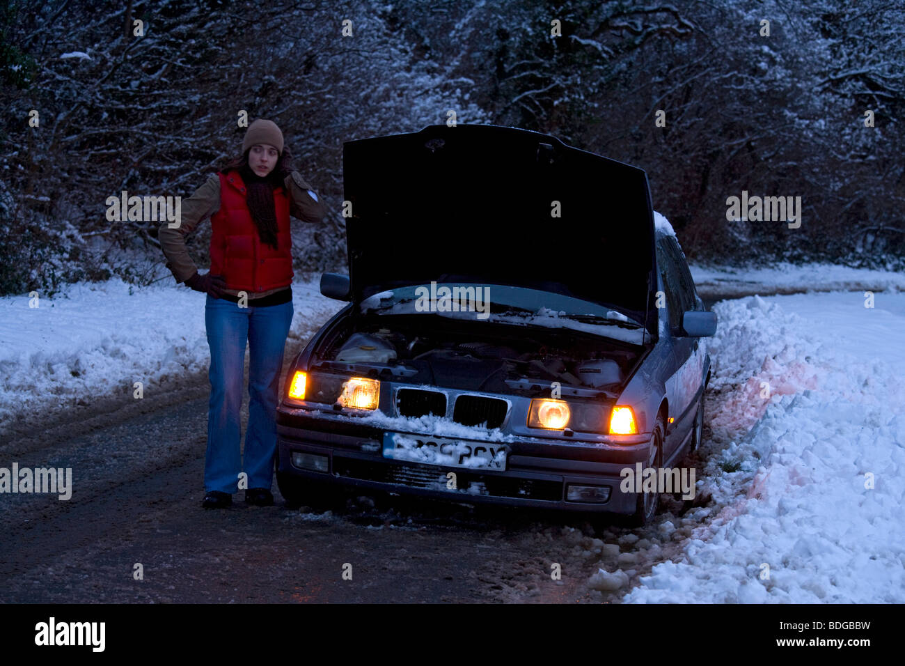 Women on her own broken down in the snow, stranded trying to get it fixed. Stock Photo