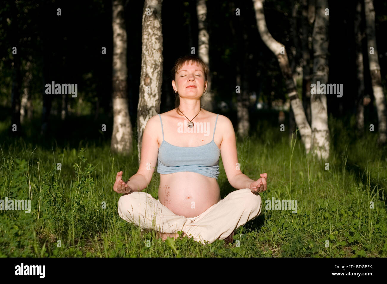 Pregnant woman sitting on grass in yoga cross-legged position Stock ...
