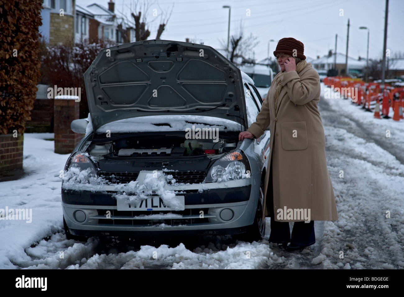 women on her own with broken down car in winter snow, bonnet up on mobile phone to breakdown recovery service Stock Photo