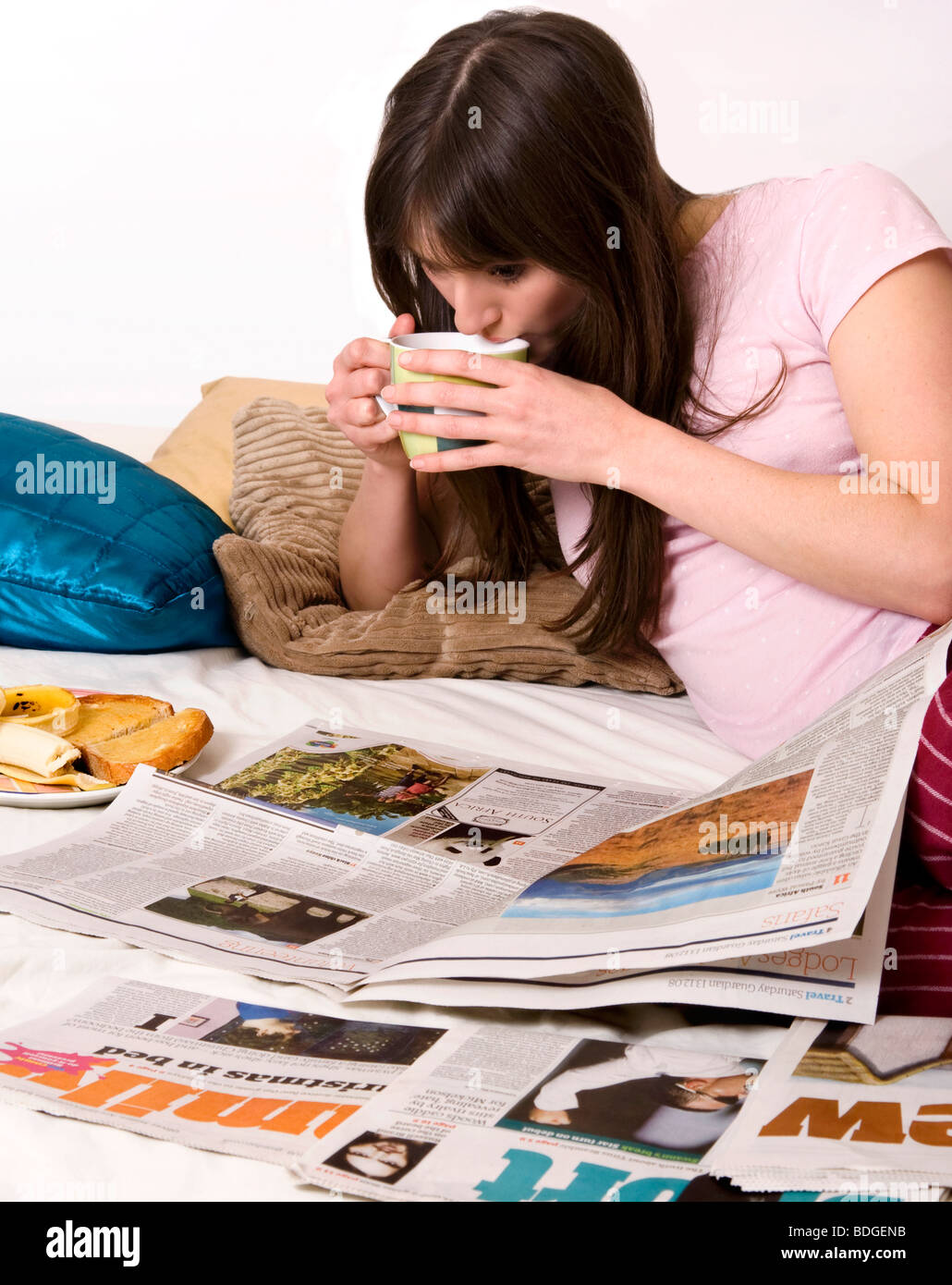 Young woman having breakfast and reading the newspaper in bed Stock Photo