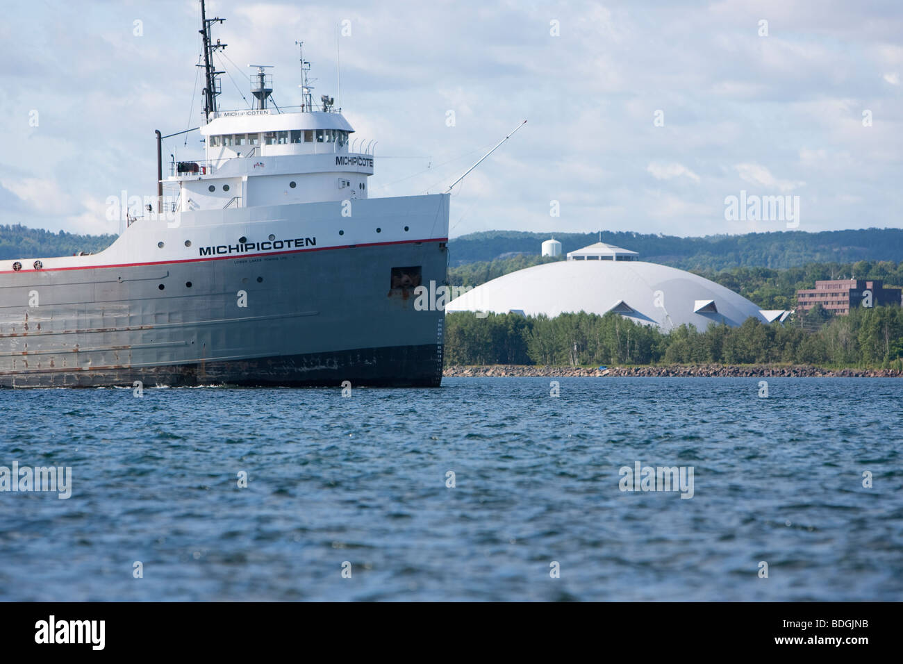 The bow of a freighter with the Superior Dome of Northern Michigan University in the background. Stock Photo
