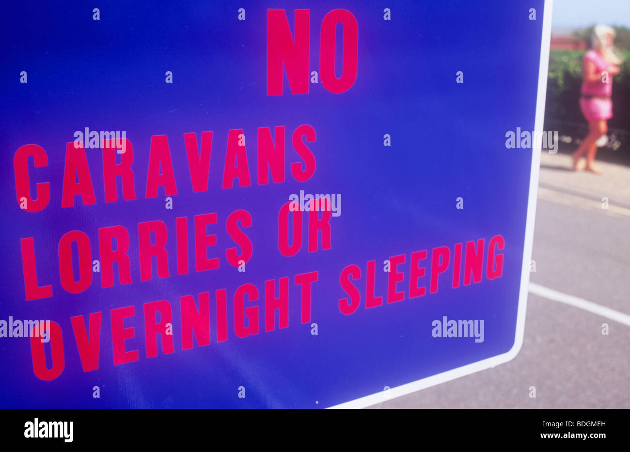 Detail of luminescent blue and red sign stating No Caravans Lorries or Overnight sleeping and with woman walking by Stock Photo