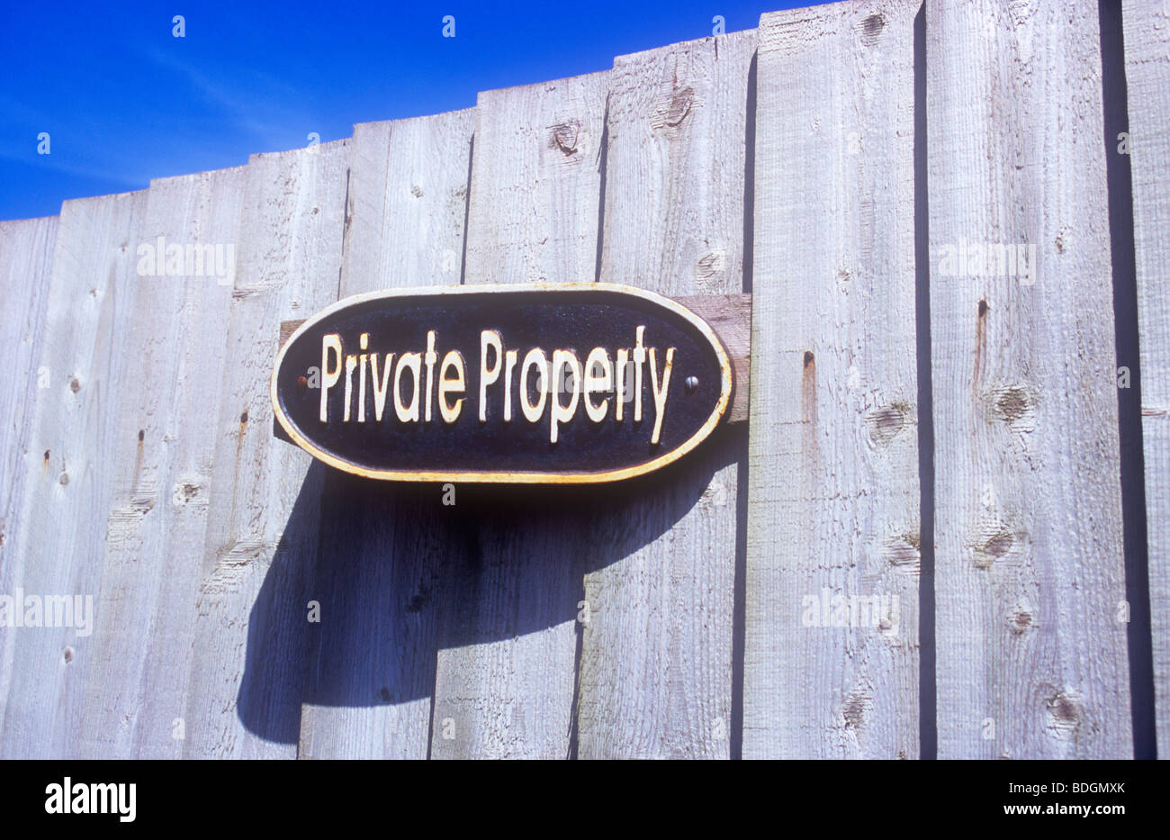 Oval cast metal sign fixed on wooden fence under blue sky casting shadow and stating Private Property Stock Photo
