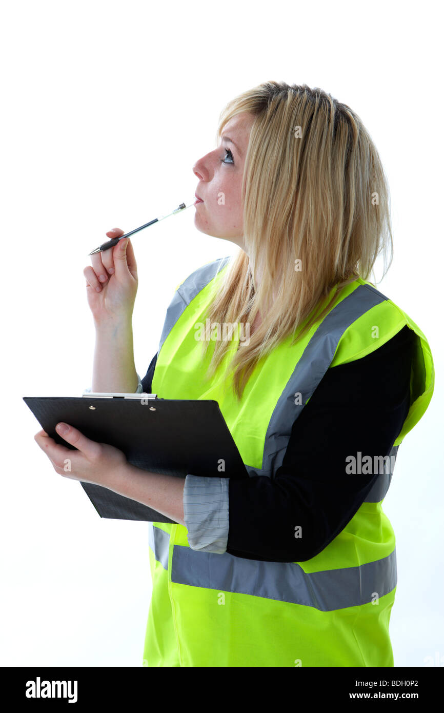young 20 year old blonde woman in high vis vest thinking looking up and chewing on the end of a pen holding a clipboard observing taking notes manager Stock Photo