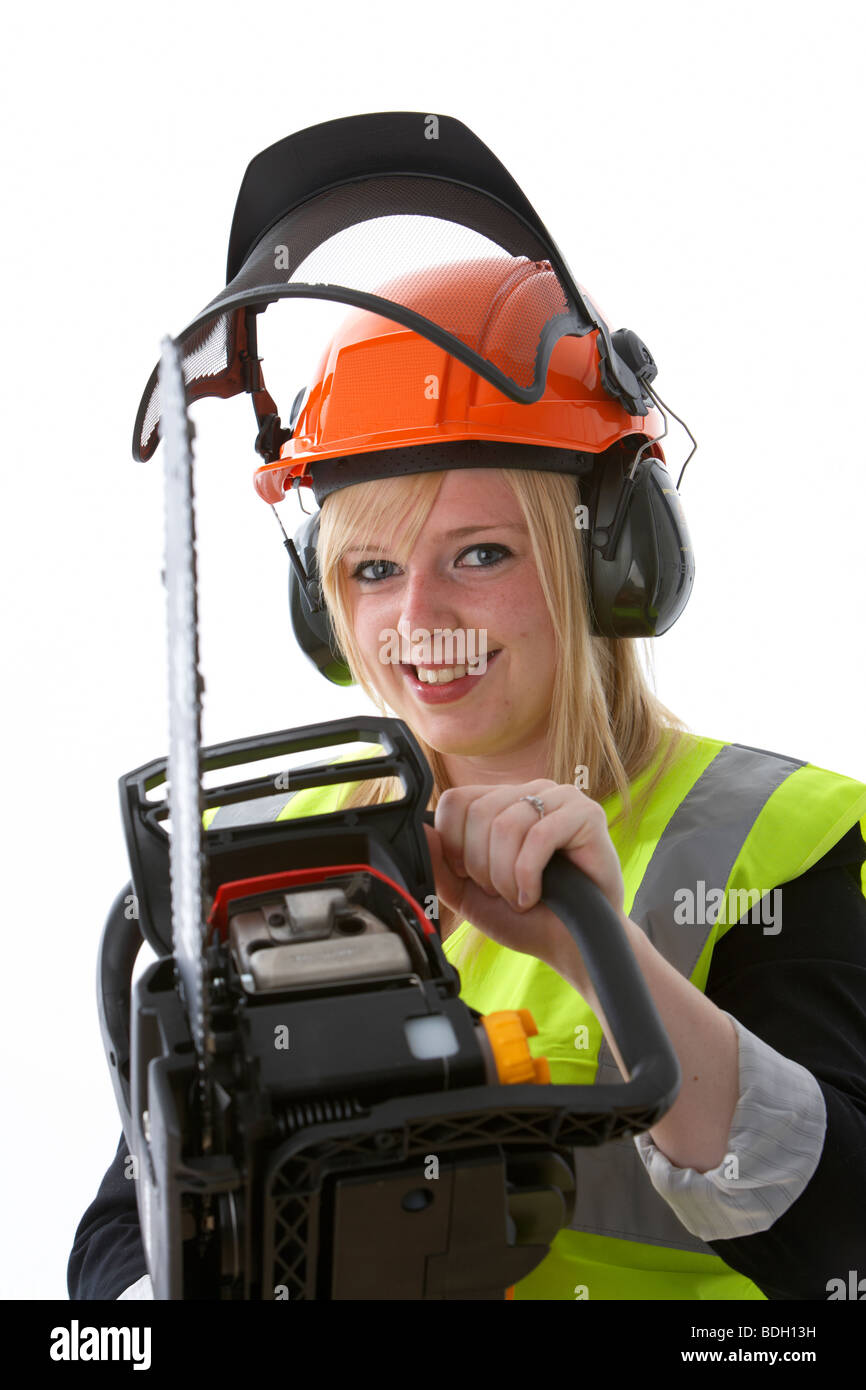 young 20 year old blonde woman wearing orange hard hat ear protectors visor and high vis vest holding chainsaw and smiling Stock Photo
