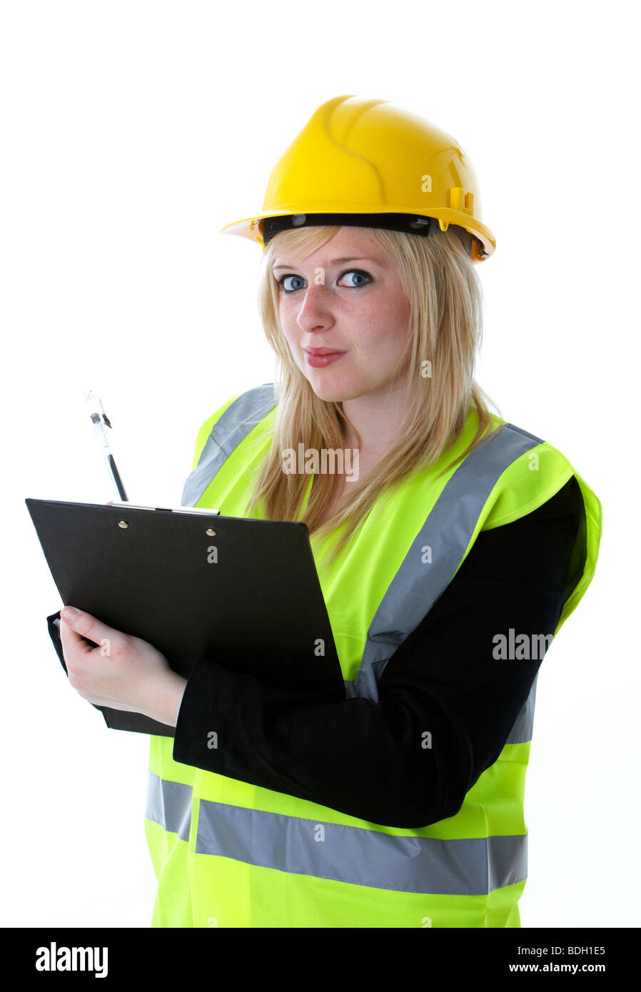 young 20 year old blonde woman wearing yellow hard hat and high vis vest writing on a clipboard with eye contact taking notes observing manager Stock Photo