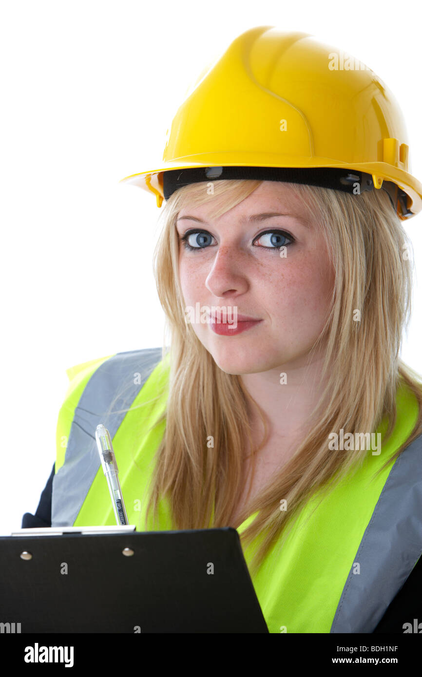 young 20 year old blonde woman wearing yellow hard hat and high vis vest writing on a clipboard with eye contact Stock Photo