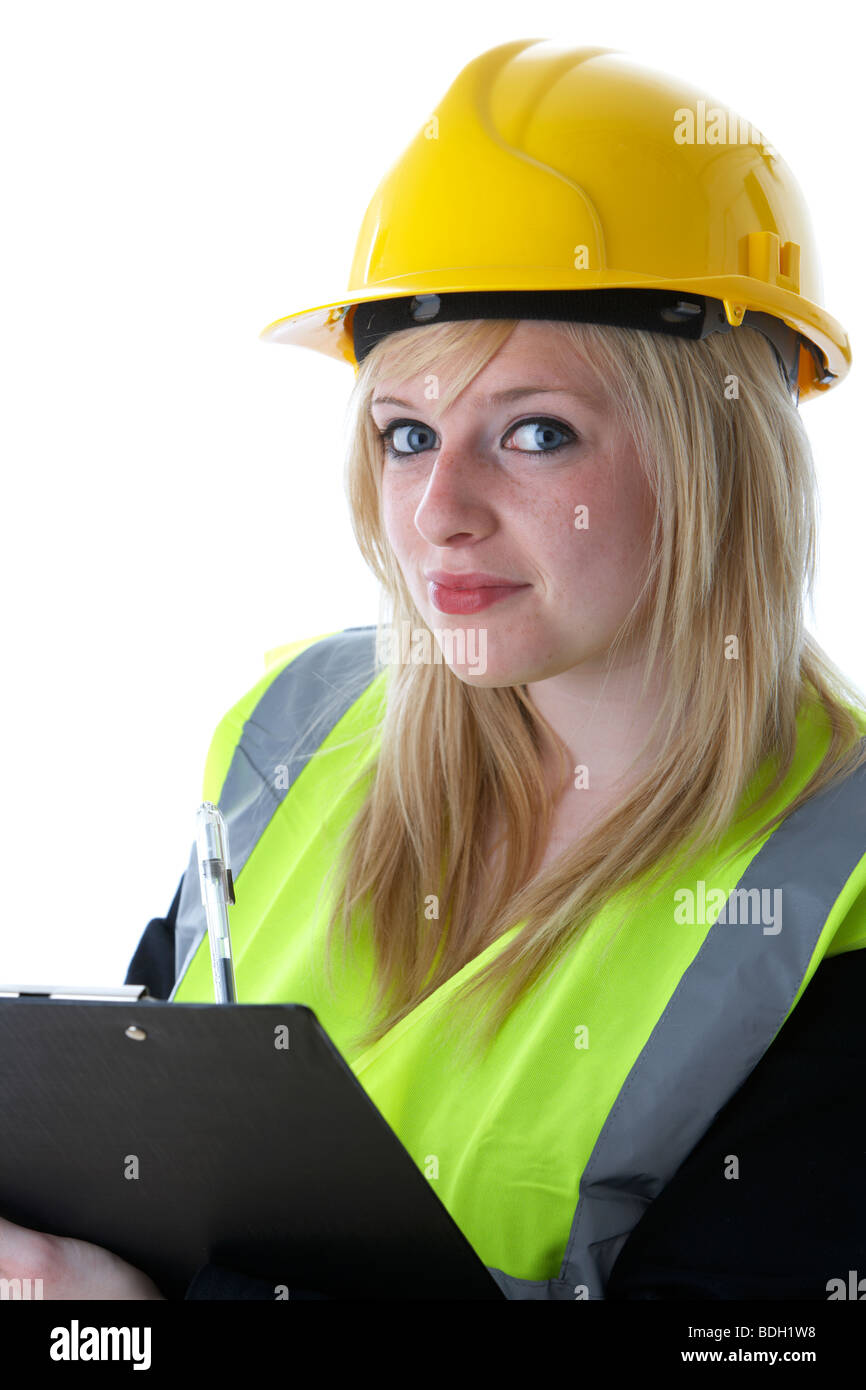 young 20 year old blonde woman wearing yellow hard hat and high vis vest writing on a clipboard with eye contact smiling Stock Photo