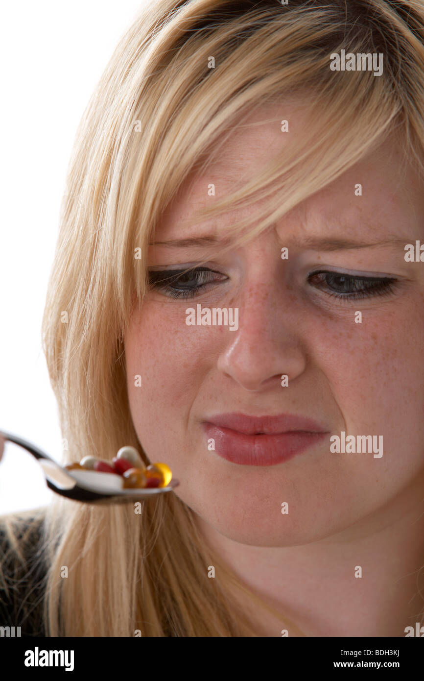 young 20 year old blonde woman with a spoonful of vitamin supplements looking disgusted Stock Photo