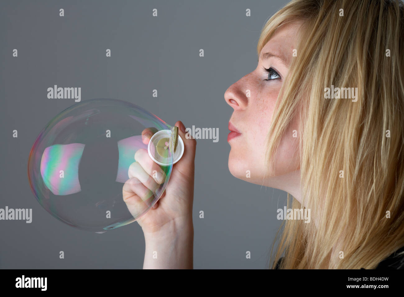 young 20 year old blonde woman blowing one large bubble from a childs toy Stock Photo