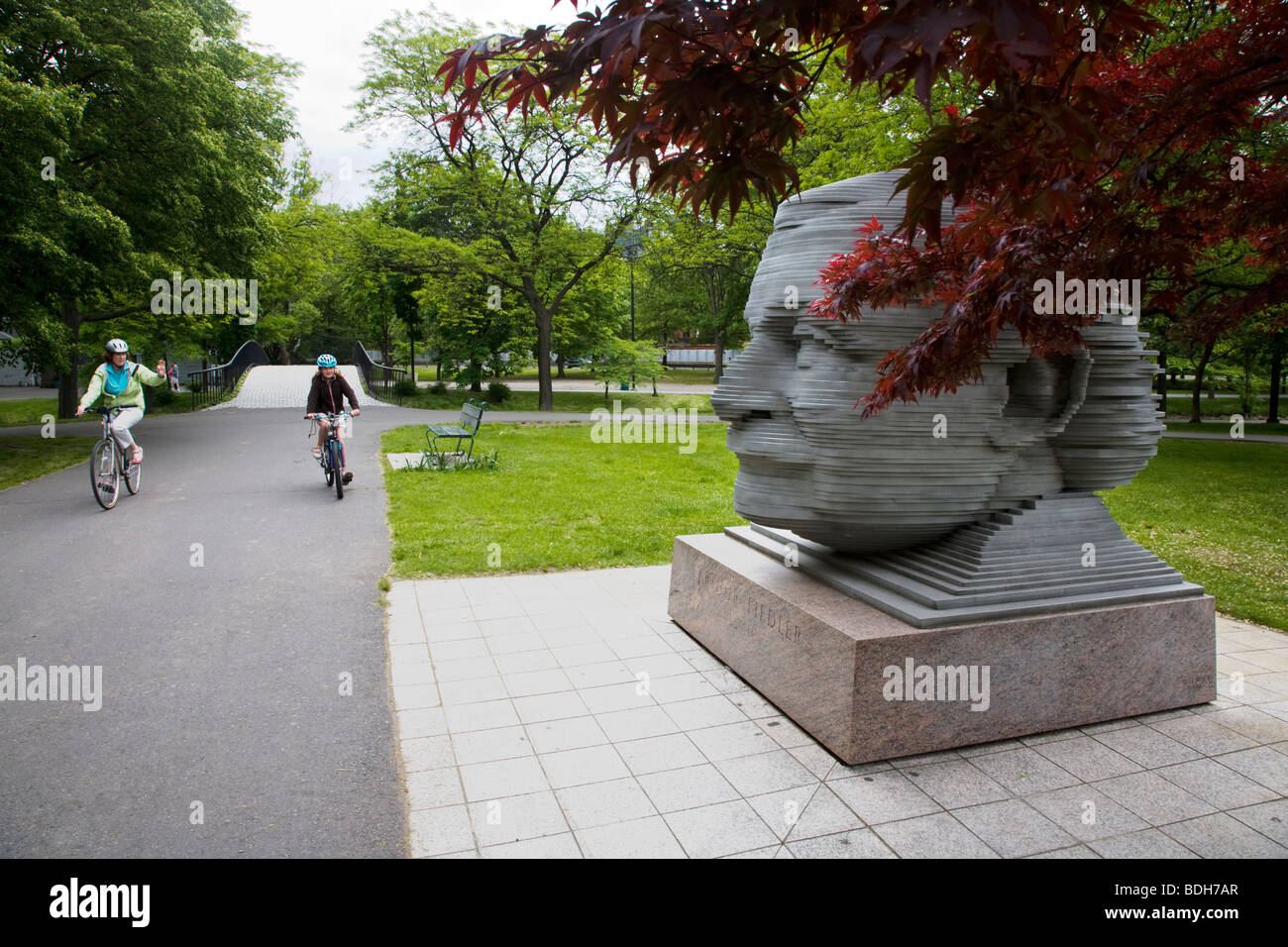 Bicyclists pass a statue of ARTHUR FIEDLER the conductor of the Boston Pops in CHARLES RIVER PARK - BOSTON, MASSACHUSETTS Stock Photo