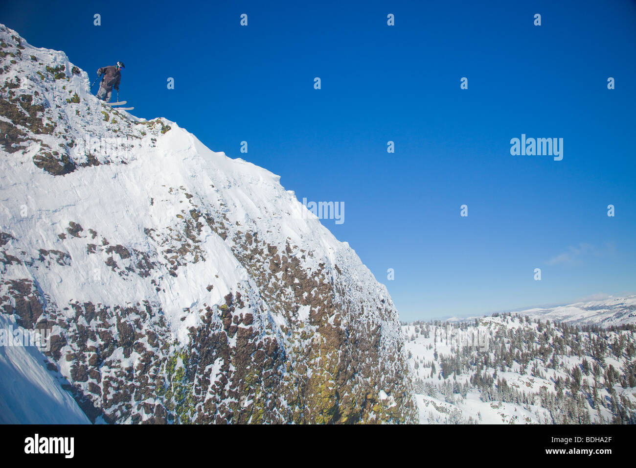 Skier overlooking a steep drop to scout his line before jumping. Stock Photo