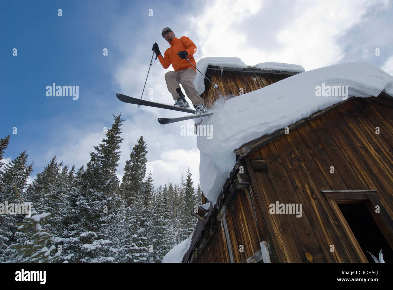A man jumping off an old mining building  roof with skis in Uncompaghre National Forest, Ouray, Colorado. Stock Photo