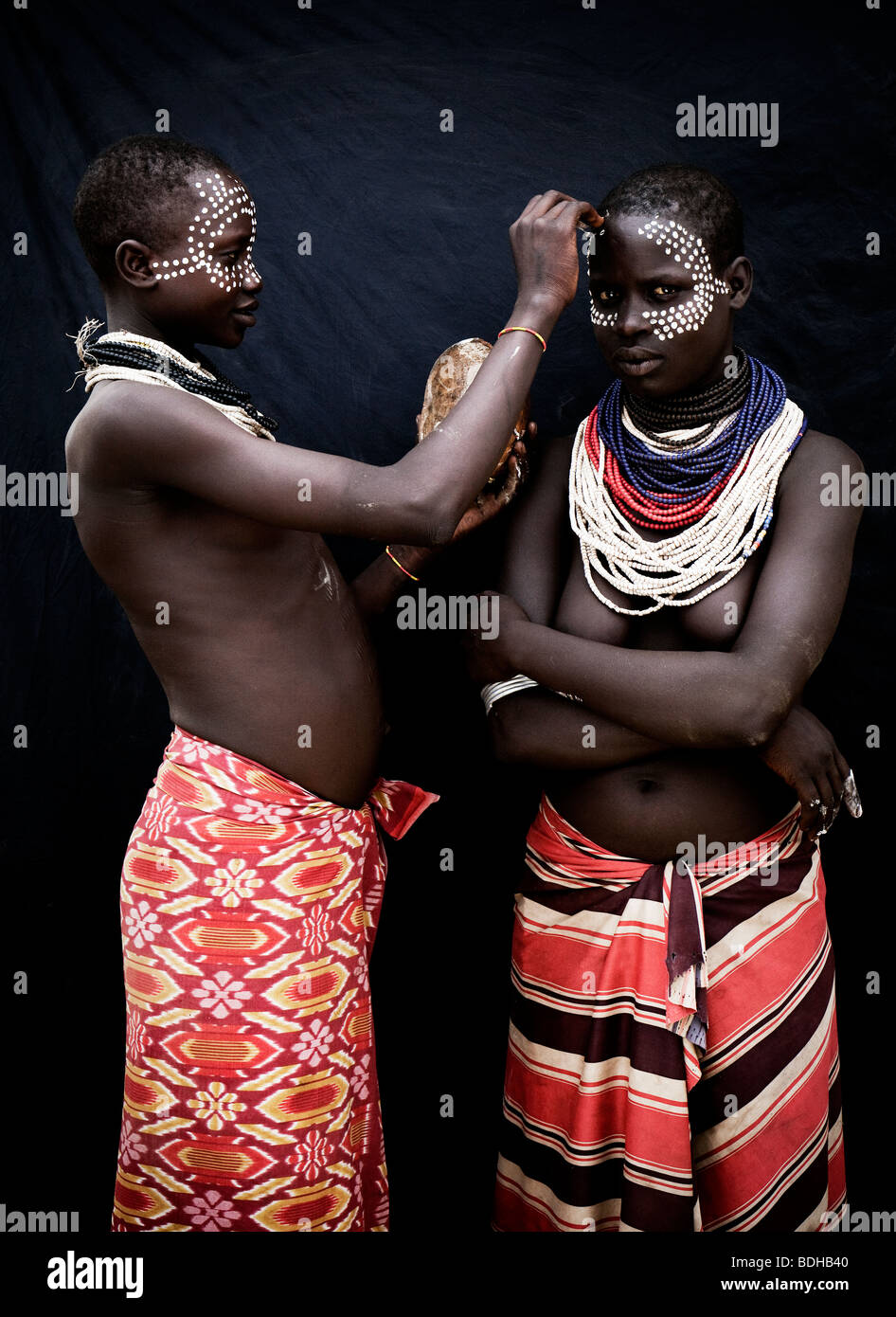 Portrait of two young women in traditional attire and body decoration posed before a black cloth. Stock Photo