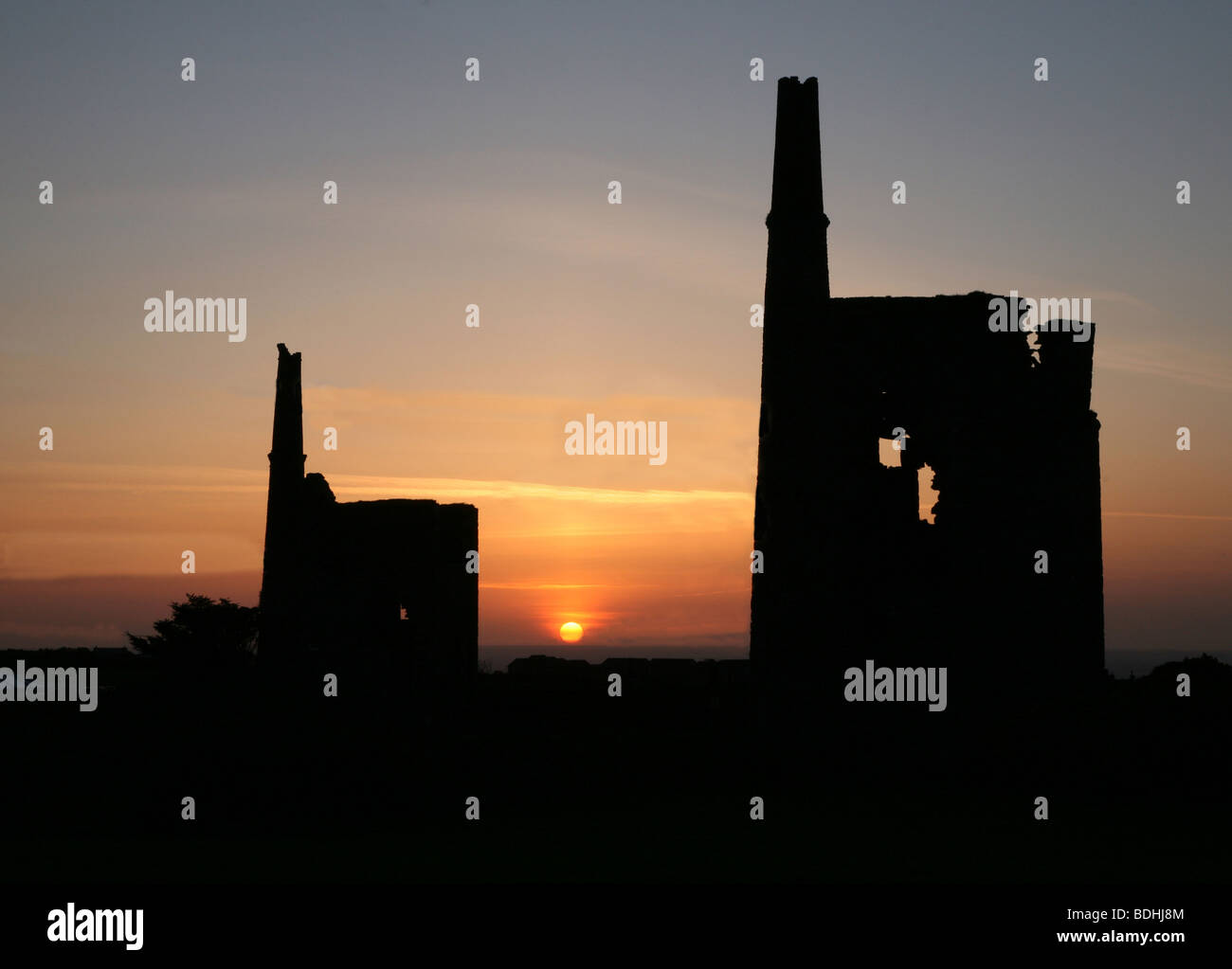 Two Cornish tin mines near to Pendeen at sun set with the sun going down in an orange sky Stock Photo