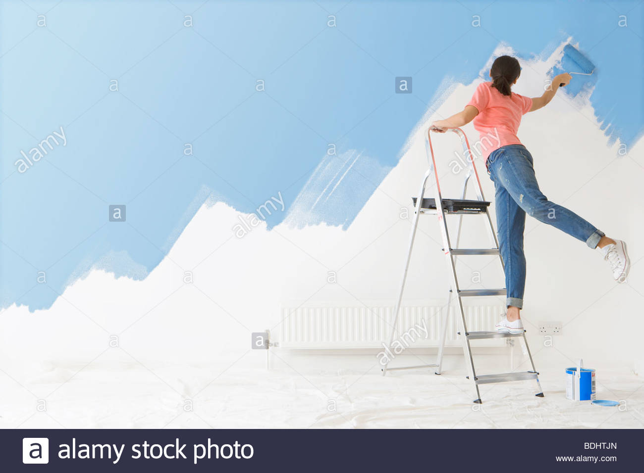 Woman On Ladder Painting Wall With Paint Roller Woman On Ladder Painting Wall With Paint Roller