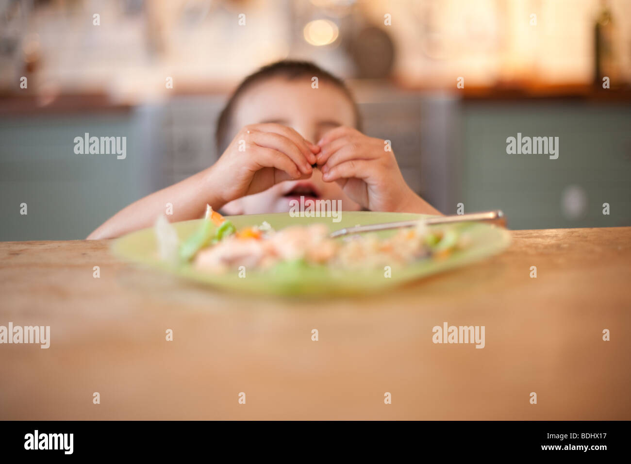3 year old boy sits ignoring his food at the dinner table Stock Photo