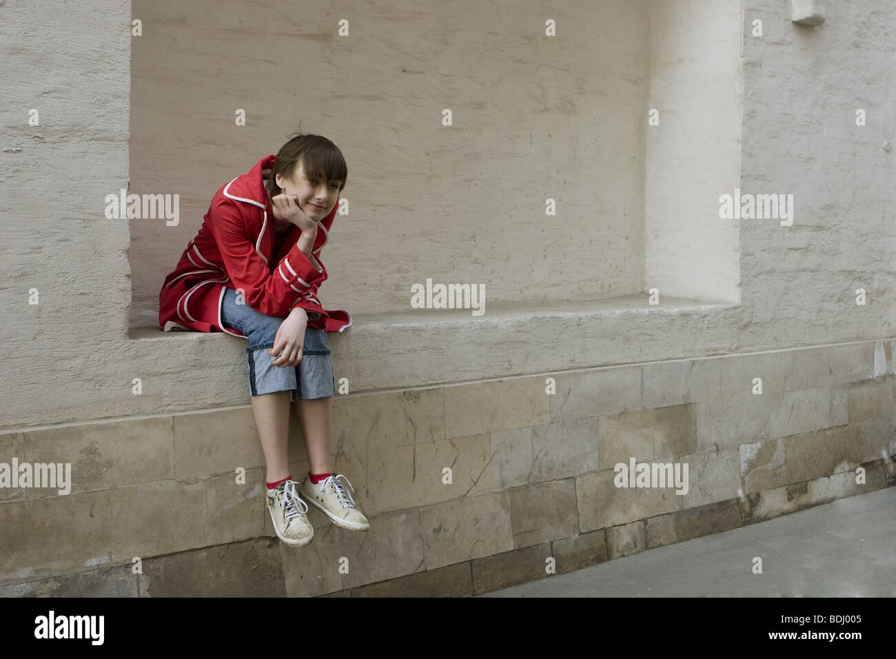 portrait of young girl sitting at the wall Stock Photo