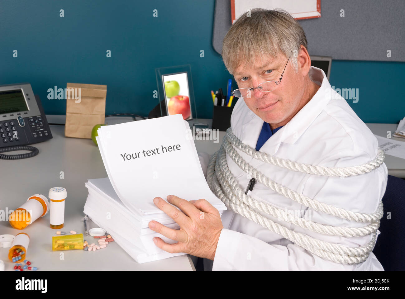A physician is tied up with a load of bureaucratic paperwork preventing him from doing his job. Stock Photo
